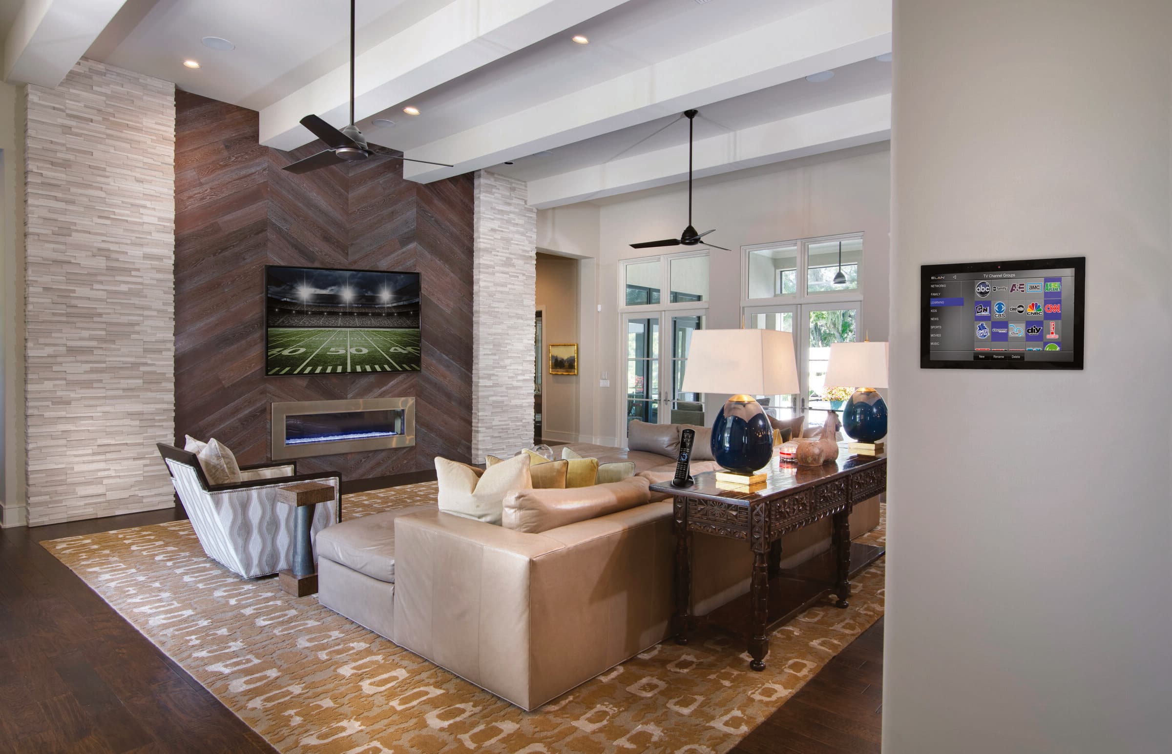 A warm living room with a media wall, wall-mounted display and touchpanel, and discreet architectural audio
