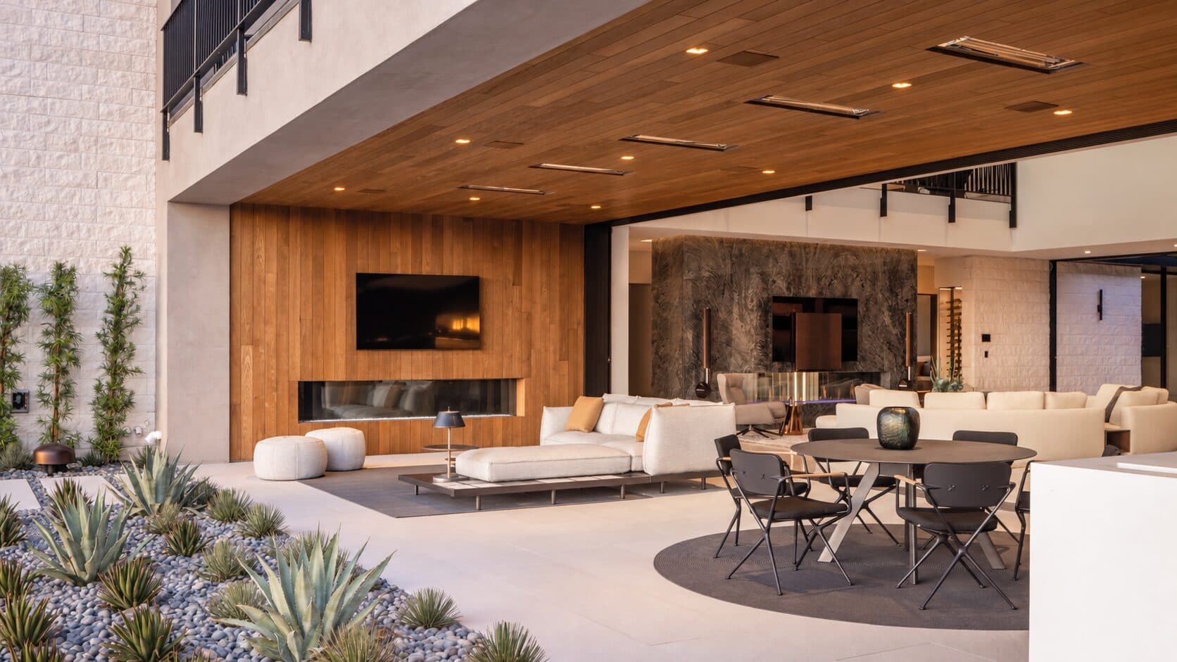A covered outdoor living room with an open wall to the terrace, fireplace, wall-mounted display, and dining area